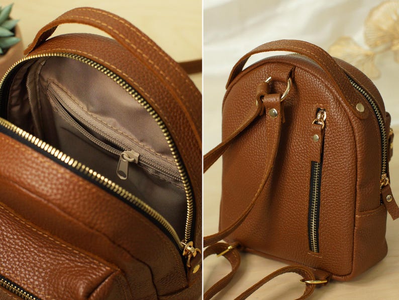 May include: A brown textured mini backpack featuring a top handle, adjustable shoulder straps, and gold-tone hardware. The interior is lined with fabric and includes a zippered pocket, while the exterior back panel features a vertical zippered pocket.