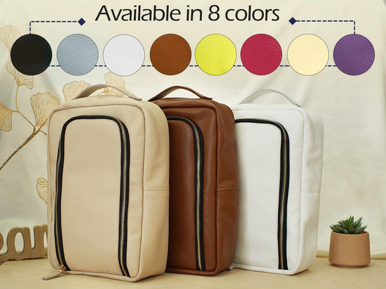 May include: Three rectangular bags with textured surfaces in beige, brown, and white. Each bag features a vertical black zippered front compartment and a top handle. The image includes text stating Available in 8 colors with circular swatches.