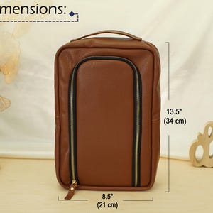 May include: A brown rectangular bag with a textured surface, a top handle, and a U-shaped black zipper closure with gold-tone hardware. The bag measures 13.5 inches in height and 8.5 inches in width as indicated by the printed dimension labels.