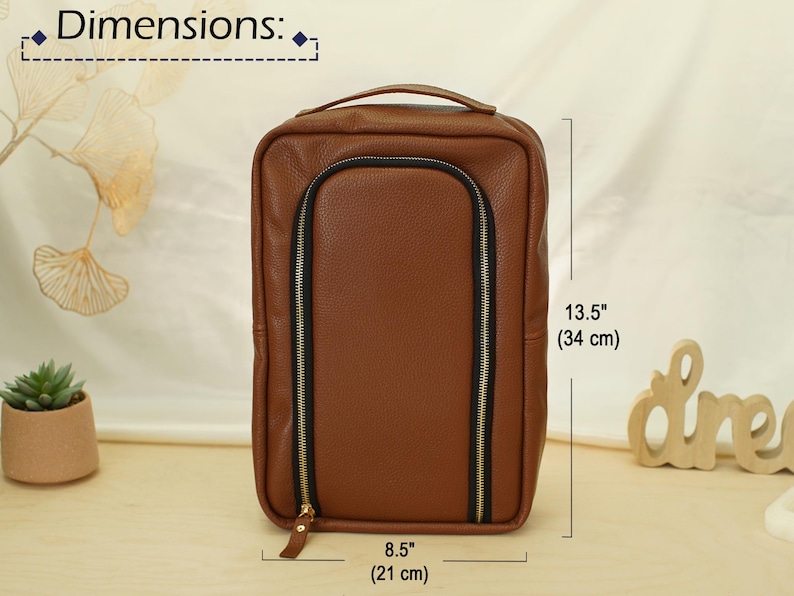 May include: A brown rectangular bag with a textured surface, a top handle, and a U-shaped black zipper closure with gold-tone hardware. The bag measures 13.5 inches in height and 8.5 inches in width as indicated by the printed dimension labels.