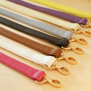 Può includere: Una collezione di cinturini da polso colorati in varie tonalità, tra cui rosa, bianco, marrone, nero, grigio, viola e giallo. Ogni cinturino è realizzato in materiale strutturato e presenta una chiusura color oro per l'attacco.