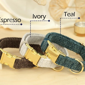 May include: Three dog collars in Espresso, Ivory, and Teal. Each collar has a gold-colored metal buckle and a matching D-ring. The collars are made of a textured fabric.