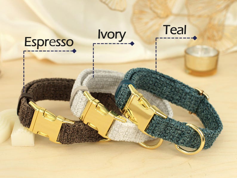 May include: Three dog collars in Espresso, Ivory, and Teal. Each collar has a gold-colored metal buckle and a matching D-ring. The collars are made of a textured fabric.