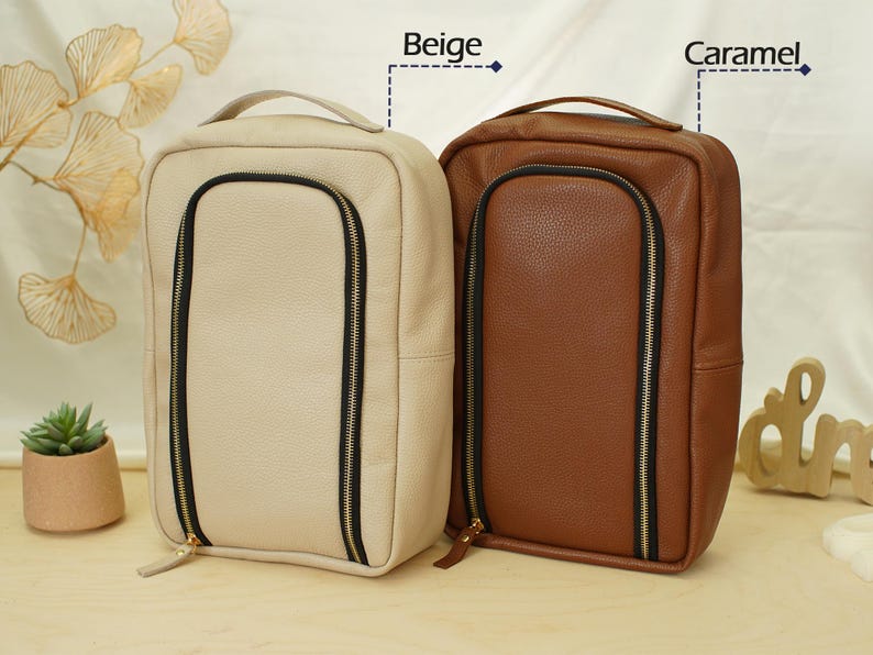 May include: Two rectangular bags with top handles and a U-shaped front zipper closure. One bag is beige and the other is caramel brown. Both feature a textured surface, black zipper tape, and gold-toned zipper pulls. The text Beige and Caramel appear.