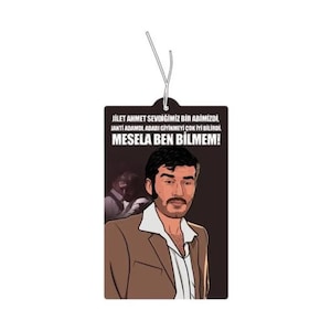 May include: Rectangular air freshener with a cartoon illustration of a man in a brown suit and white shirt. The air freshener has text in Turkish. A white string is attached for hanging.