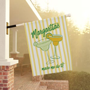 Peut inclure: Drapeau rectangulaire extérieur à rayures jaunes et blanches. Il présente deux verres à margarita et l'inscription "Margaritas made me do it!" en vert. Le drapeau est suspendu à l'extérieur.