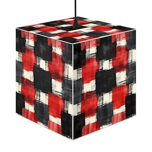 Puede incluir: Lámpara colgante cúbica con un patrón abstracto y audaz. El diseño presenta grandes pinceladas superpuestas en rojo, negro y blanco roto. La lámpara cuelga de un cable negro, mostrando una estética moderna y artística.