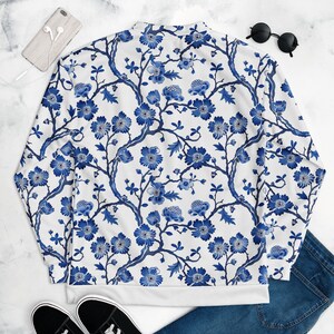 May include: A white bomber jacket with a blue and white floral pattern. The jacket has a stand-up collar and a zipper closure.