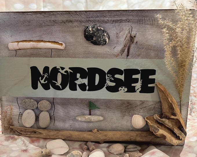 Diese Nordsee Deko ist eine Holz Deko zum aufhängen mit einem kleinen Steinbild und Strandfunde dekoriert.