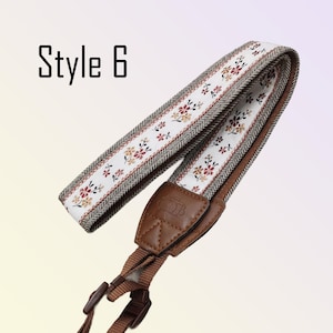 May include: A camera strap with a floral pattern on a white background, bordered by a brown and cream herringbone design. The strap has brown leather and adjustable brown nylon straps. The text "Style 6" is in the upper left corner.