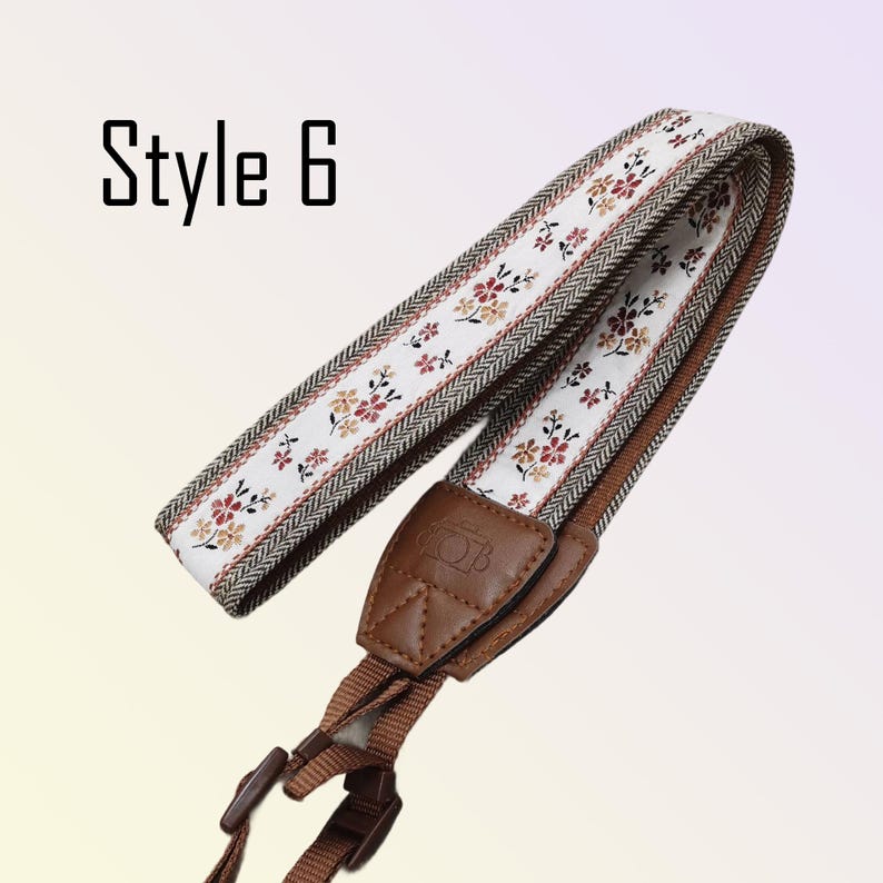 May include: A camera strap with a floral pattern on a white background, bordered by a brown and cream herringbone design. The strap has brown leather and adjustable brown nylon straps. The text "Style 6" is in the upper left corner.
