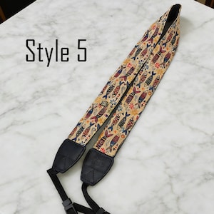 May include: Camera strap with a beige background and a repeating pattern of colorful fish and floral designs. The strap has black leather ends and the text "Style 5" is visible.