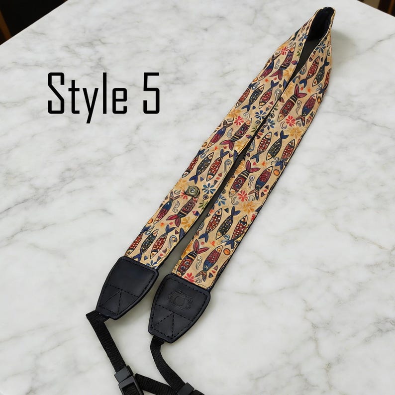 May include: Camera strap with a beige background and a repeating pattern of colorful fish and floral designs. The strap has black leather ends and the text "Style 5" is visible.