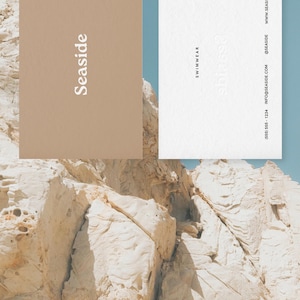 May include: Two business cards with the text "SeaSide" and "Swimwear" on them. The cards are on a background of white and tan rock formations.
