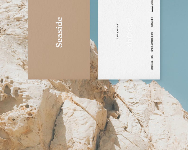 May include: Two business cards with the text "SeaSide" and "Swimwear" on them. The cards are on a background of white and tan rock formations.