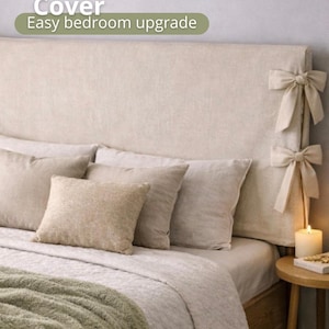 Puede incluir: Funda de cabecero beige con lazos decorativos. La funda del cabecero se combina con almohadas y ropa de cama a juego. El texto de la imagen dice "Headboard Cover Easy bedroom upgrade". Una vela encendida está sobre una mesita de noche de madera.