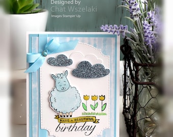 May include: A handmade greeting card featuring a light blue sheep illustration, three yellow tulips, and two dark grey glitter clouds. The card includes a light blue ribbon bow and a banner with the text HAVE A BEAUTIFUL birthday.