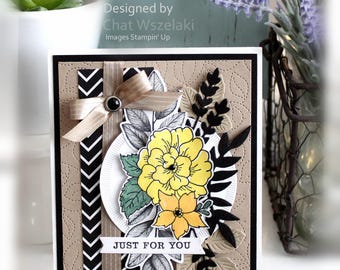 May include: A rectangular greeting card featuring a tan embossed leaf background, a black and white chevron strip, a beige ribbon bow with a black gem, and a central floral arrangement with yellow flowers and black die-cut foliage. Text reads: JUST FOR YOU.