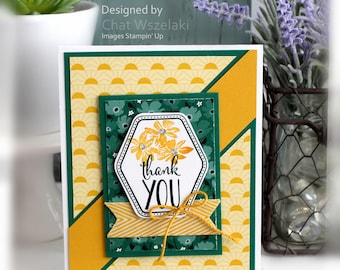 May include: A rectangular greeting card featuring a yellow sunburst pattern, a dark green floral panel, and a central hexagonal white label with the text "thank YOU" in black script. The card is accented with yellow flowers and a yellow twine bow.