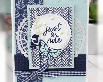 May include: A blue and white card with a butterfly and the text "just a note" in a circle. The card is decorated with a white doily and a blue and white gingham ribbon.