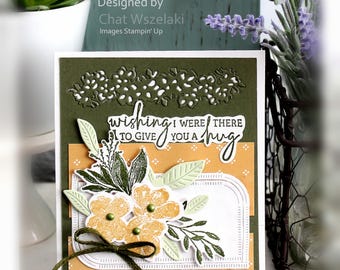 May include: A rectangular greeting card featuring an olive green background with a mustard yellow panel patterned with white dots. The card displays a die-cut floral arrangement in yellow and green, a dark green twine bow, and the text "wishing I WERE THERE TO GIVE YOU A hug".