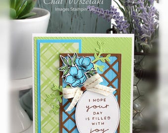 May include: A handmade greeting card featuring a light green textured background, a blue plaid panel, and a brown lattice frame. It includes a blue floral illustration, a beige ribbon bow, and an oval tag with the text I HOPE your DAY IS FILLED WITH joy.