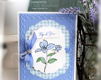 May include: A handmade greeting card featuring a light blue embossed border, a white scalloped layer with a blue gingham pattern, and a central white panel displaying a hand-drawn blue flower with green leaves and the text Thank You with a blue ribbon.