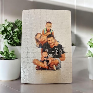Könnte beinhalten: Ein weißes Puzzle mit einem Foto einer vierköpfigen Familie. Der Vater sitzt auf dem Boden und hat seine beiden Söhne in den Armen. Der jüngste Sohn sitzt auf dem Schoß des Vaters, während der ältere Sohn hinter dem Vater steht und seine Arme um den Hals des Vaters legt. Die Mutter steht hinter dem Vater und dem älteren Sohn und hat ihren Arm um den Hals des älteren Sohnes gelegt.