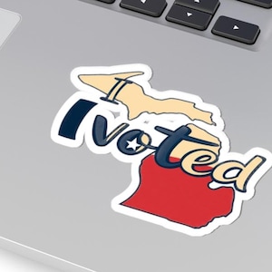 Peut inclure: Un autocollant découpé représentant l'État du Michigan en beige et rouge, avec le texte I Voted en lettres bleu foncé. La lettre O est remplacée par une étoile blanche sur un cercle bleu, et l'autocollant est posé sur un clavier d'ordinateur portable.