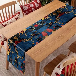 Peut inclure: Un chemin de table rectangulaire présentant un motif patchwork bleu foncé avec des motifs floraux dorés en volutes, des accents rouges et de petits points dorés circulaires. Le chemin est posé à plat sur une table en bois clair.