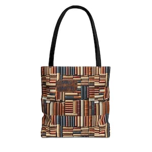 Peut inclure: Un sac fourre-tout avec des anses noires et un motif répétitif de livres empilés dans des tons marron, beige et gris. Un écusson rectangulaire aspect cuir marron est centré sur le devant avec le texte MRS SMITH imprimé en lettres capitales bleu foncé.
