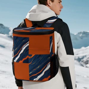Peut inclure: Un sac à dos rectangulaire au design color-block, composé de panneaux orange brûlé unis et de sections à motifs marbrés bleu foncé, orange et blanc. Le sac comprend des poches latérales en filet noir et des bretelles réglables.