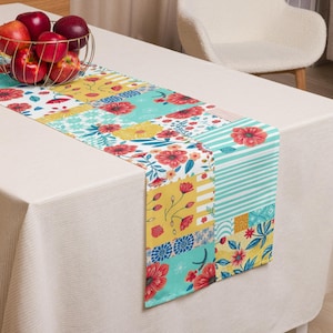 Peut inclure: Un chemin de table rectangulaire présentant un motif patchwork de fleurs dans des tons rouge, jaune et bleu sarcelle. Le tissu affiche diverses sections avec des fleurs rouges, des fonds jaunes et des rayures sarcelle sur une nappe claire.