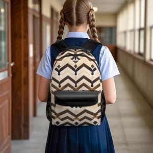 Peut inclure: Un sac à dos arborant un motif chevron répétitif dans des tons marron foncé, marron clair et crème. Le sac comprend une poche avant noire unie, des bretelles noires et des poches latérales en filet noir, avec une poignée et des fermetures éclair.