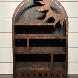 Puede incluir: Una estantería de madera con un diseño de sol y luna. La estantería tiene varios compartimentos y una fila de fases lunares en la parte inferior.