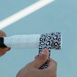 May include: A person is wrapping a white and black leopard print grip tape around the handle of a black paddle.