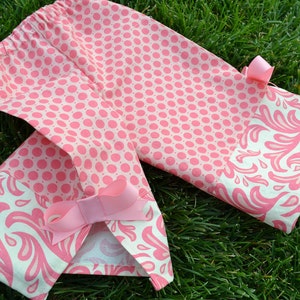 May include: Pink fabric shorts with a white and pink floral pattern on the bottom hem. The shorts have a pink polka dot pattern on the top half and a pink bow on the side.