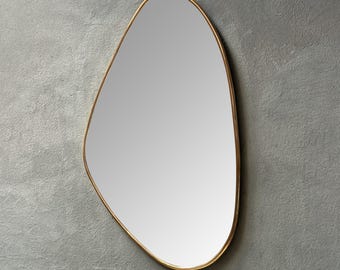 May include: An irregularly shaped mirror with a gold-colored metal frame. The mirror's reflective surface is smooth and clear, set against a gray background. The frame has a thin profile, adding a modern touch to the design.