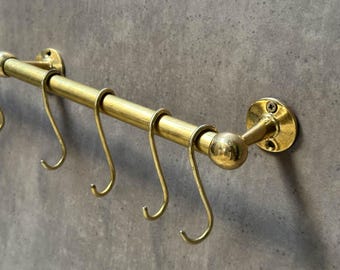May include: Brass pot rack with five hooks. The rack is mounted to a wall with a round base and a decorative ball finial.