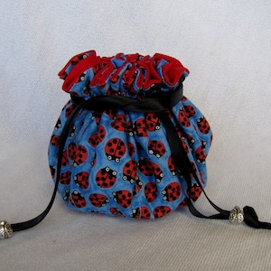May include: A blue drawstring bag with a black ribbon closure and ladybug print. The bag has two black ribbon ties with silver metal beads at the ends.