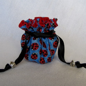 May include: A blue fabric drawstring bag with a red trim and a ladybug print. The bag has black ribbon ties with silver bead accents.