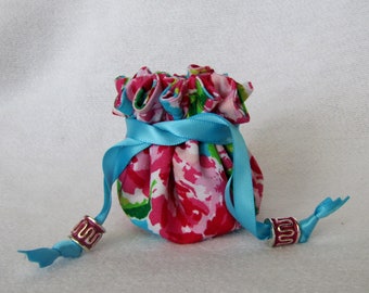May include: A small pink and green floral drawstring bag with a blue ribbon and silver and pink bead accents.