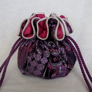May include: A purple drawstring bag with a pink and white floral pattern. The bag has a white trim and a long purple cord.