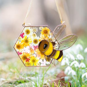 stained glass bee suncatcher with pressed flowers in honeycomb shape on white background