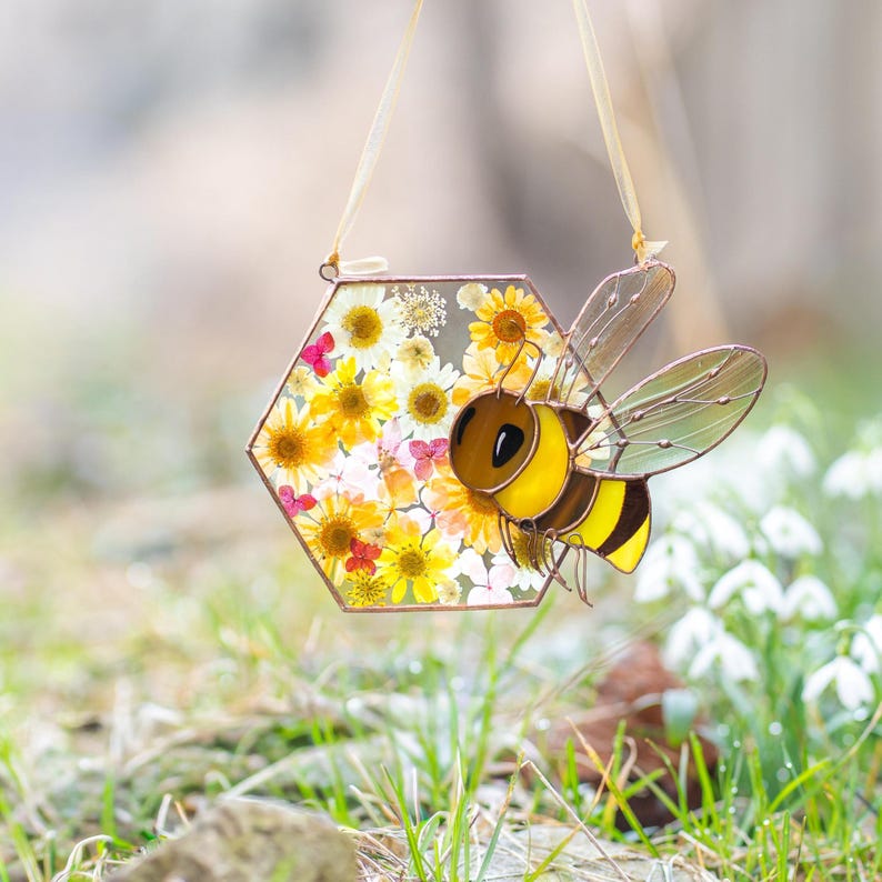 stained glass bee suncatcher with pressed flowers in honeycomb shape on white background