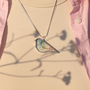 Pressed flower jewelry with bird silhouette and soft natural textures.