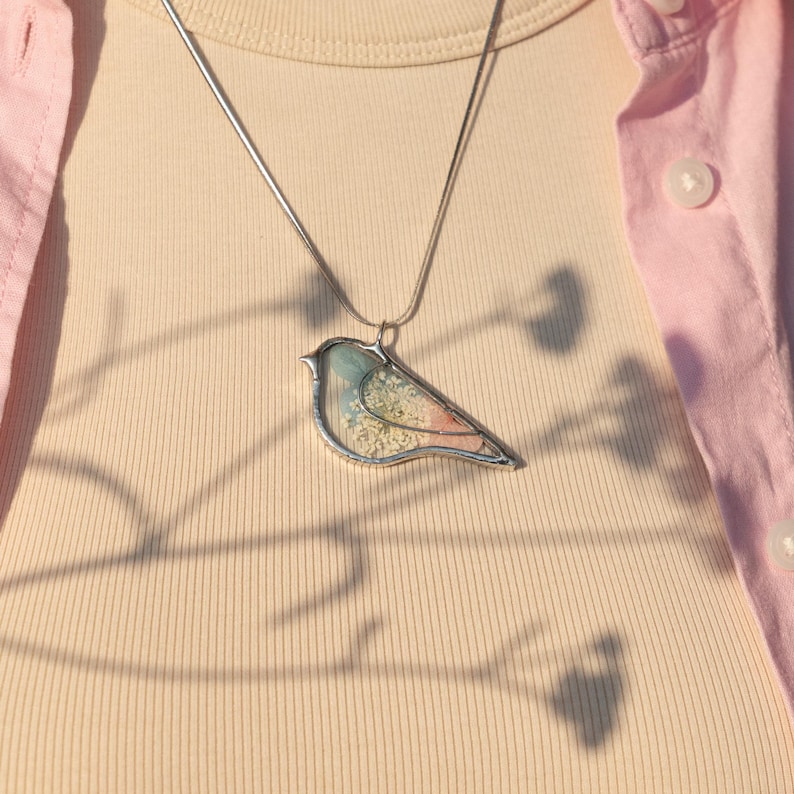 Pressed flower jewelry with bird silhouette and soft natural textures.