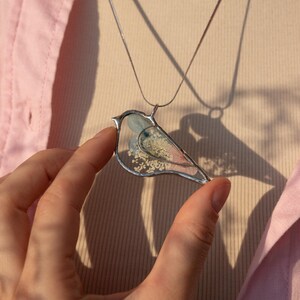 Bird pendant hanging in sunlight with preserved flowers inside.