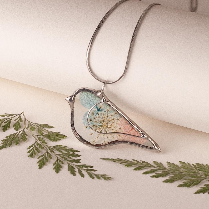 Dainty bird necklace with stained glass frame and botanical details.