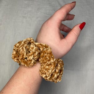 Può includere: Un elastico per capelli in velluto marrone con una texture morbida e soffice. L'elastico è legato intorno a un polso.